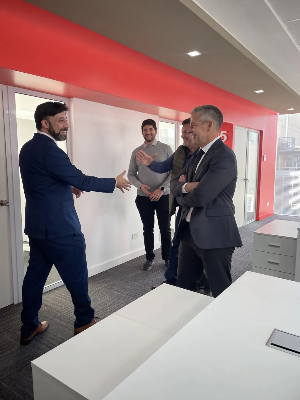Cuatro personas conversan de pie en el pasillo de una oficina, al comienzo de la visita.