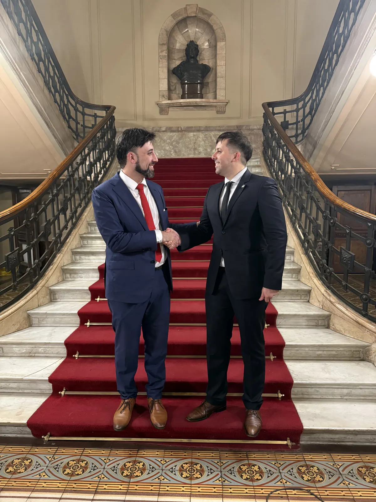 Saludo entre representantes de dos organizaciones en una escalera institucional
